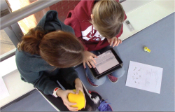 Capture d'écran 1. sur la passerelle, on voit Louise et le citron antistress, Rori et l'iPad, la feuille de consignes, un magnétophone et une petite figurine à côté de la feuille. On ne voit pas la chercheuse (moi) qui filme l'extrait en question, caméra en main (enregistrement vidéo du 5 février 2019).